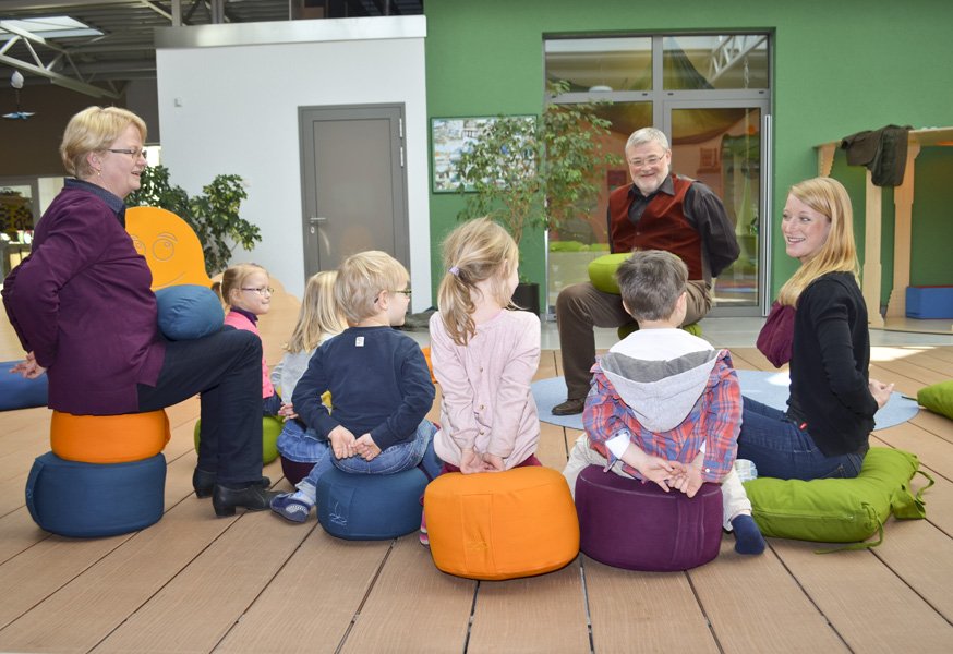 Erzieher und Kinder sitzen auf Bodenkissen im Sitzkreis