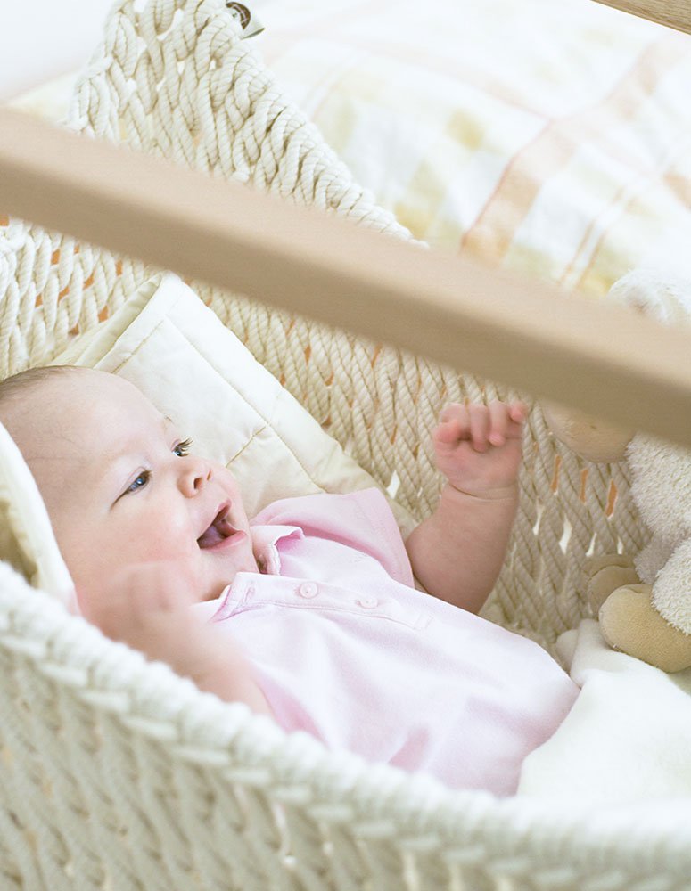 Ein Baby im Babyschwinger neben dem Elternbett